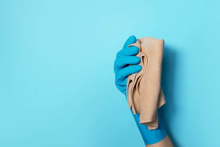 Hand in glove holding microfiber cleaning cloth on blue background. Copy space. Cleaning service concept. Spring general or regular clean up. Commercial cleaning company concept