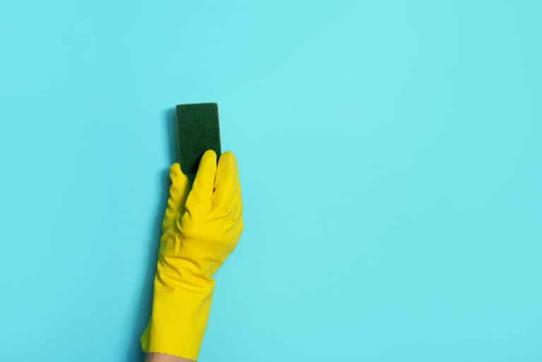 Hand in glove holding microfiber cleaning cloth, sponge on blue background. Copy space. Cleaning service concept. Spring general or regular clean up. Commercial cleaning company concept