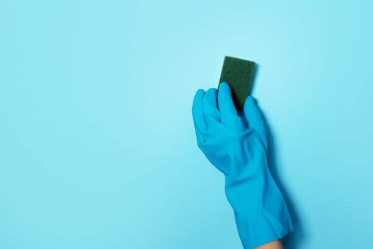 Hand in glove holding microfiber cleaning cloth, sponge on blue background. Copy space. Cleaning service concept. Spring general or regular clean up. Commercial cleaning company concept